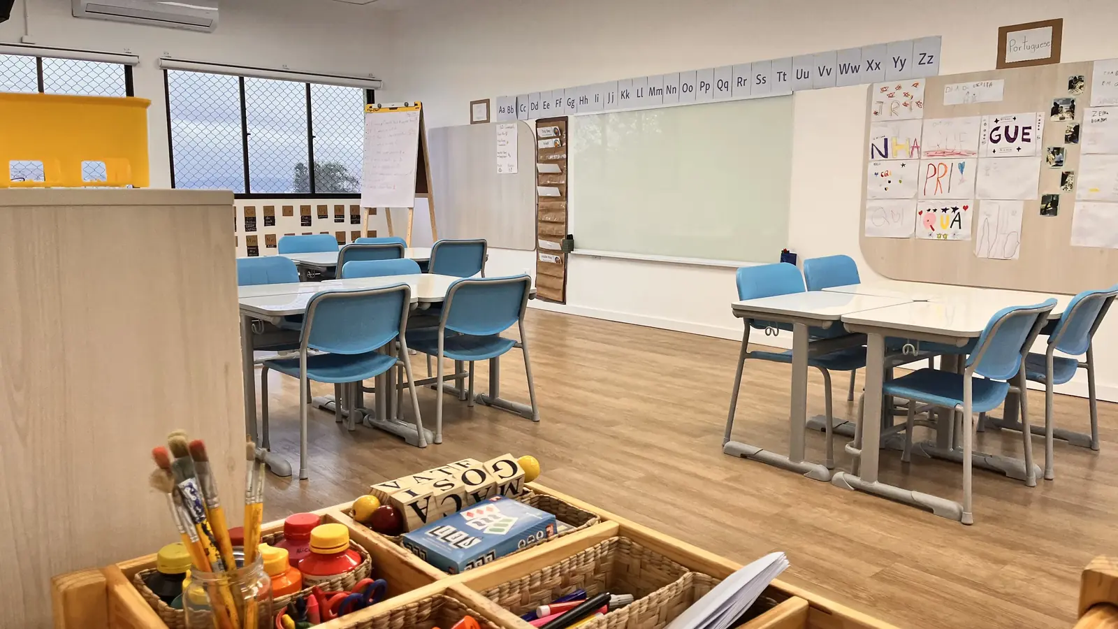 Sala de aula com mesas agrupadas, alfabeto na parede e cartazes produzidos pelas crianças.