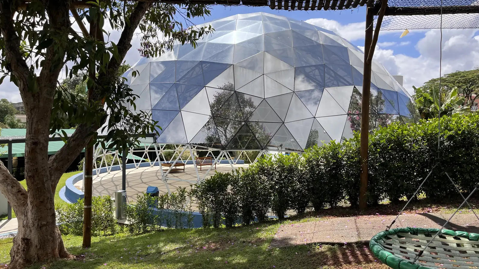 A geodésica de vidro cercada por jardim, com um balanço de ninho em primeiro plano.