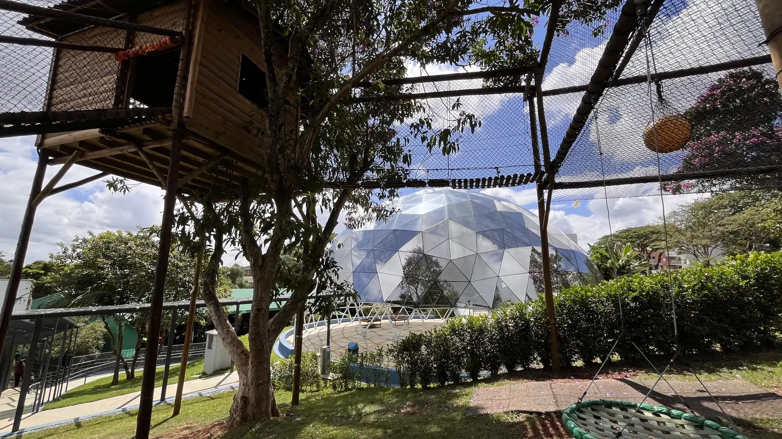 A geodésica vista por entre a casa da árvore, o jardim e as árvores do campus.